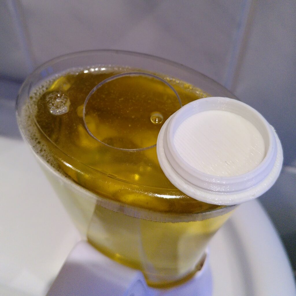 An automatic soap dispenser. A hole was drilled in the top. To close the hole again, a printed cap lies next to it.