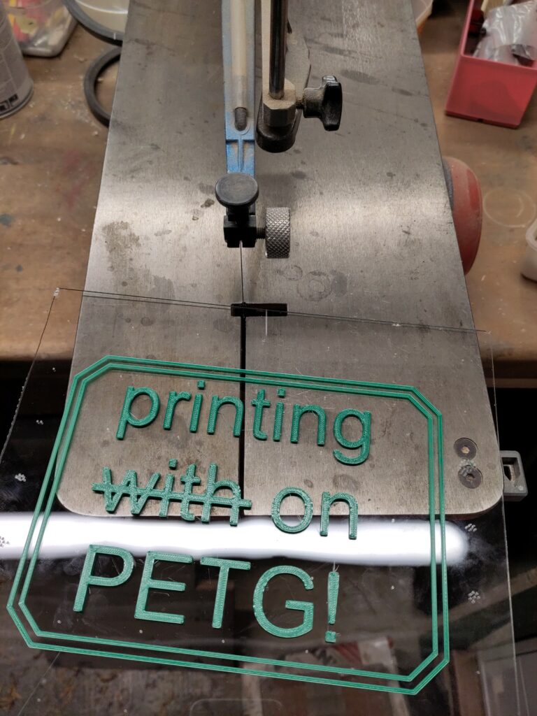 A sheet with 3d printed text on it, laying on the tabel of a scroll saw.