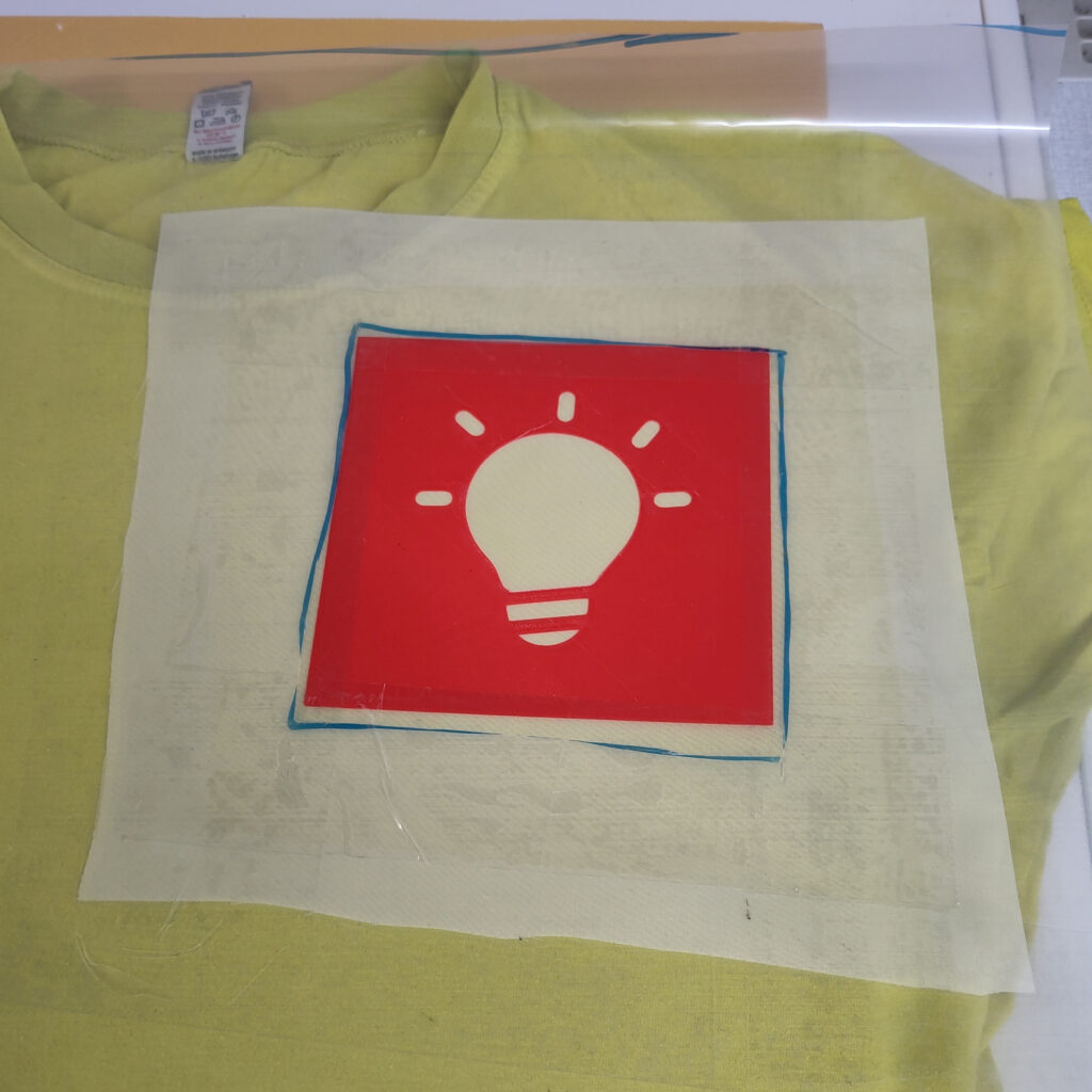The finished stencil printed on silk screen and glued to PE foil, lying on top of an T-Shirt, ready for screen printing